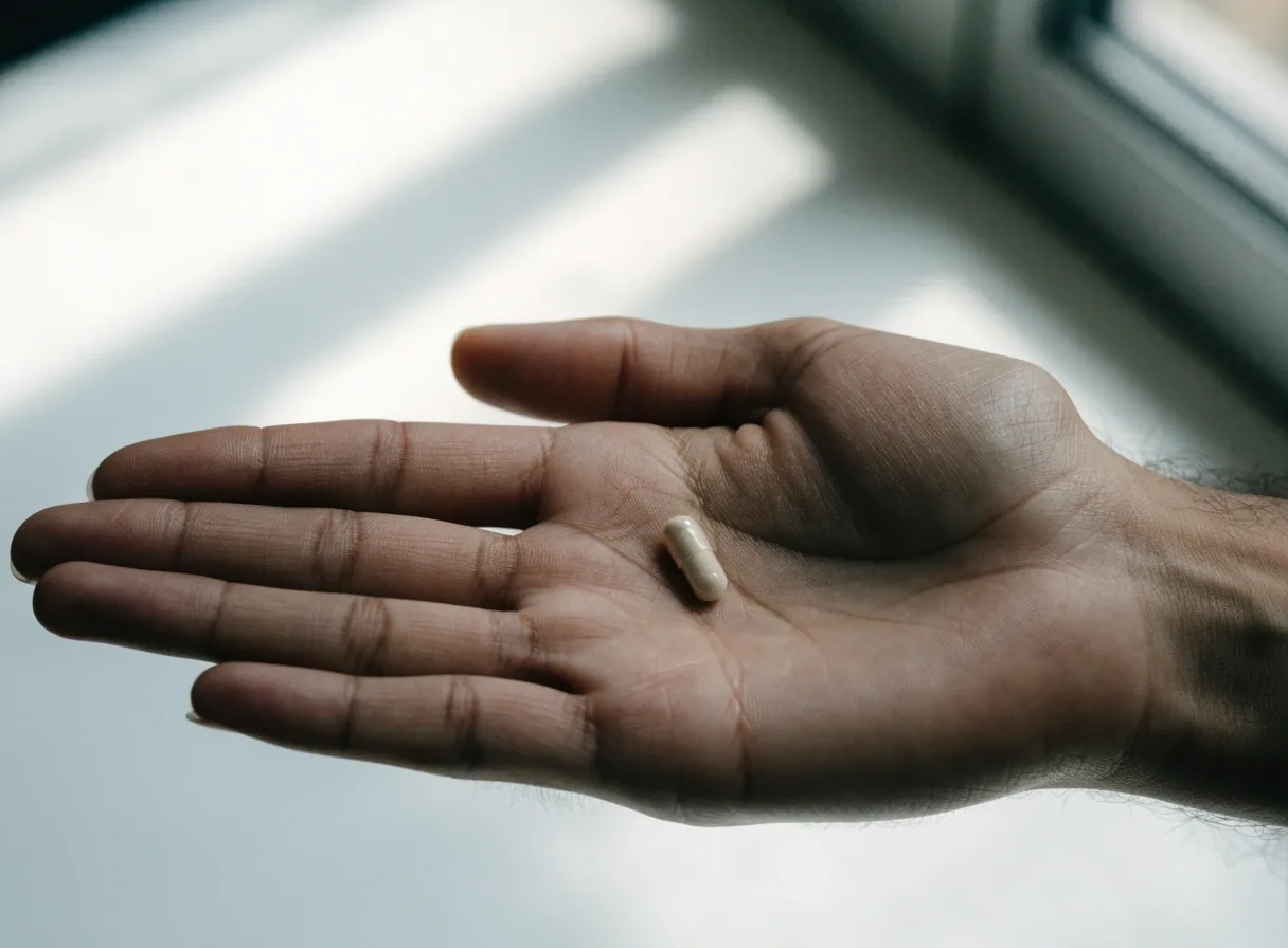 Une gélule non marquée posée dans la paume d'une main, sur un fond de table clair